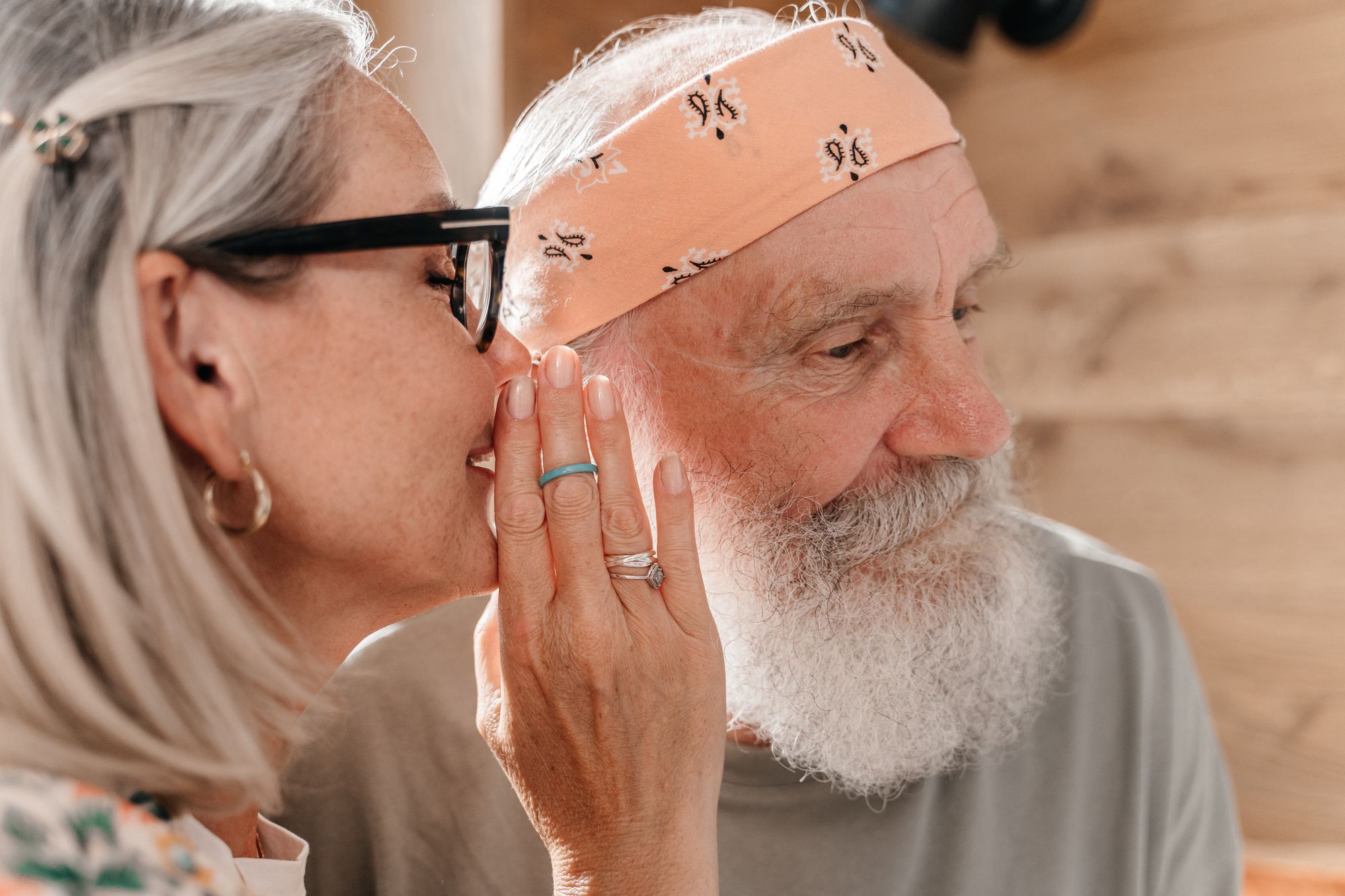 An older woman leaning in to speak close to an older man's ear while he cups his hand behind it to listen.