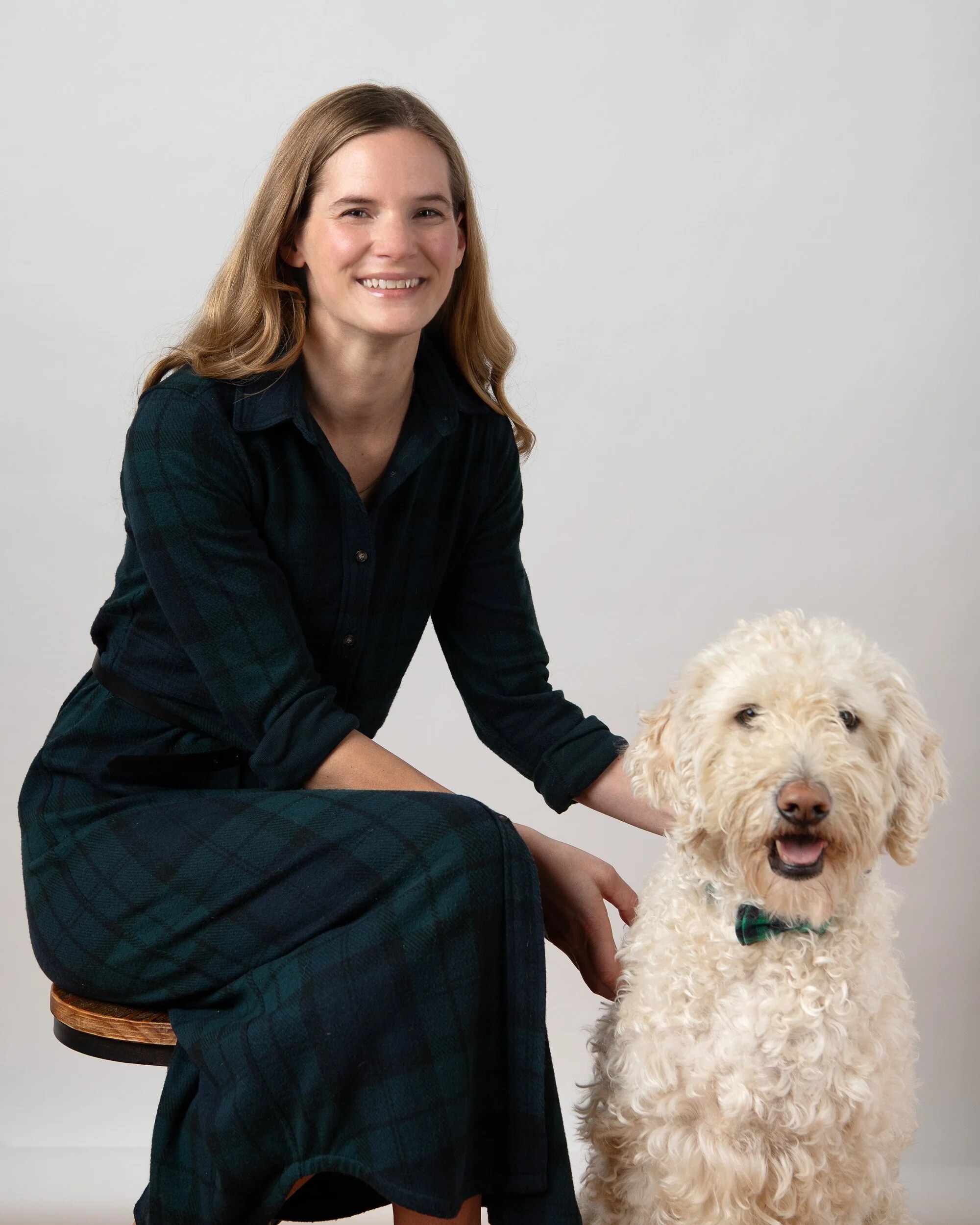 Dr. Jamie Loschen seated beside Gordon, her cream goldendoodle, who wears a tartan bow tie.